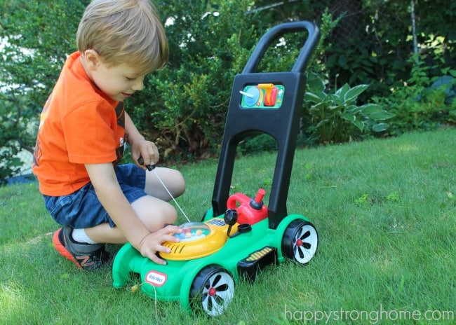 boy outdoors playing with toy lawn mower