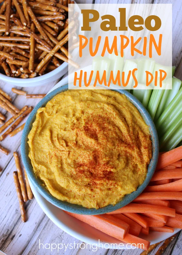 a bowl of pumpkin hummus dip with veggie sticks and pretzels next to it