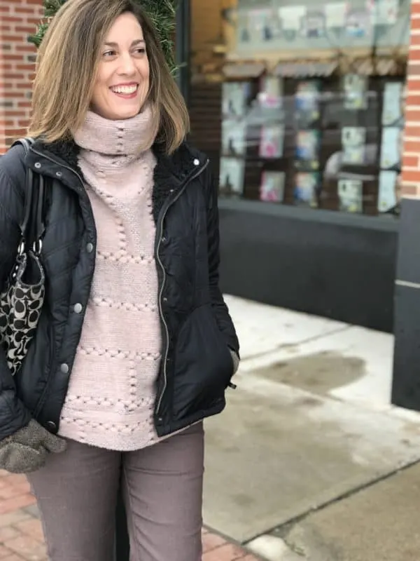 A woman wearing a black coat and pink sweater standing on a sidewalk