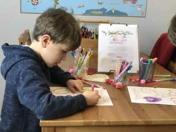 A young boy sitting at a table coloring a Valentine\'s worksheet