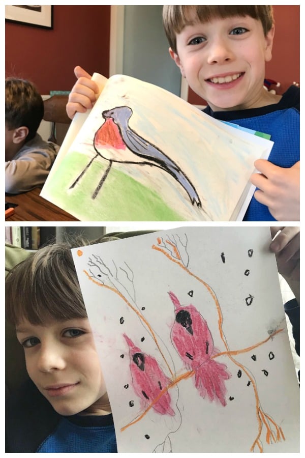 A little boy looking at the camera, holding drawings of chalk pastel birds