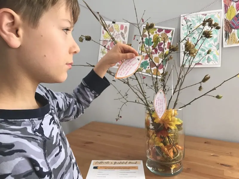 A child attaching paper leaves to branches in a vase on a table