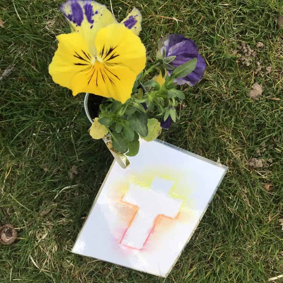 A flower that is sitting on the grass with an Easter Cross card attached