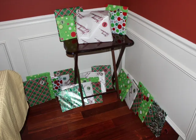 Christmas read-aloud books wrapped in Christmas gift wrap individually, arranged on a table and along the wall on the floor.