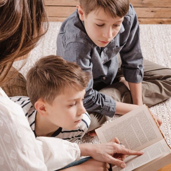 parent reading book to children on a rug