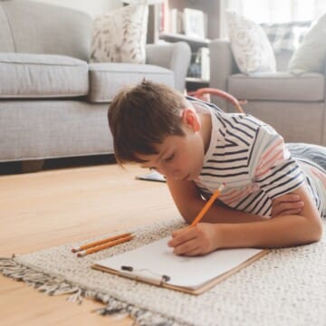 Student lying on the floor writing at home on a clipboard