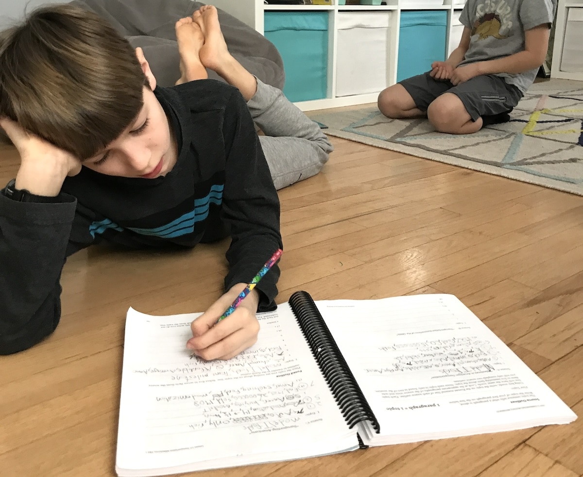 student writing in workbook on the floor, Teaching writing at home can happen anywhere